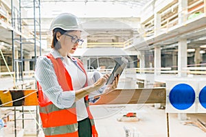 Portrait of adult female builder, engineer, architect, inspector, manager at construction site. Woman with plan, digital tablet