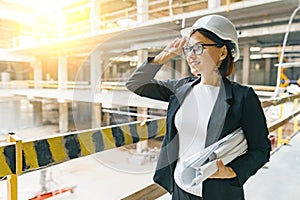 Portrait of adult female builder, engineer, architect, inspector, manager at construction site. Woman with plan, looking at