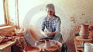 Portrait of adult female potter working with clay on pottery wheel in atelier