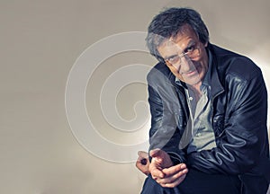 Portrait of an adult gray-haired man in glasses sitting with a questioning look on a chair in a light gray shirt and