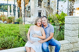 Portrait of adult happy hugging pregnant family, couple posing during walk in the city park. Fertility concept. Sunset light. soft