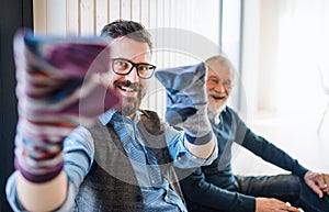 Portrait of adult hipster son and senior father sitting on floor indoors at home, having fun.