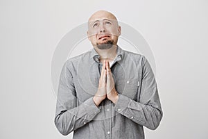 Portrait of adult male looking sad and miserable holding his hands in pray over white background. Poor man in casual