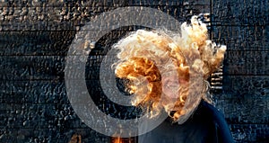 Portrait of adult mature happy laughing woman in front of burned black, wooden wall, the fiery hair covers the face, long curly