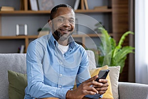Portrait of adult mature man, African American man smiling and looking at camera with phone in hand, happy sitting on