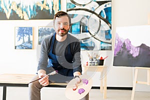 Portrait of an adult painter sitting next to his large canvas