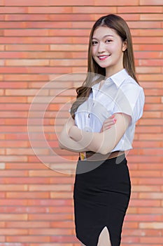 Portrait of an adult Thai student in university student uniform. Asian beautiful girl standing with her arms crossed on a brick