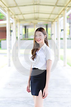 Portrait of an adult Thai student in university student uniform. Asian beautiful young girl standing smiling happily at university