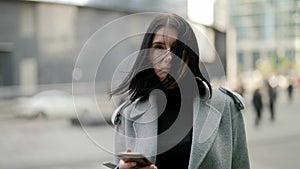 portrait of adult townswoman in city centre in autumn day, brunette lady is holding cell phone photo