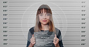 Portrait of adult woman with forelock holding sign for photo in police department. Crop view of pretty female criminal