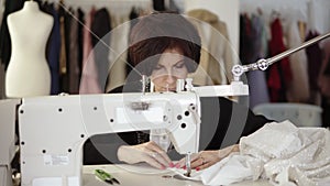 Portrait of an adult woman seamstress works at a sewing machine, working on a white hand made dress. Fashion clothes and