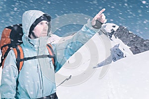 Portrait of adventurous young man on winter mountain top view pointing out.