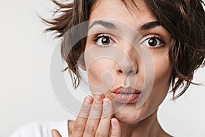 Portrait of affable woman with short brown hair in basic t-shirt covering her mouth with hand