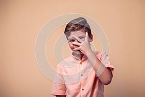 A portrait of afraid kid boy covering his face with hand. Children and emotions concept