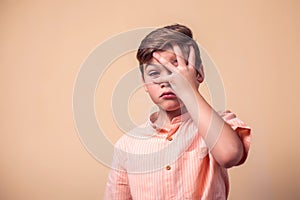 A portrait of afraid kid boy covering his face with hand. Children and emotions concept