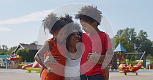 Portrait of African-American-American-american mother and preschool children hugging at outdoors playground