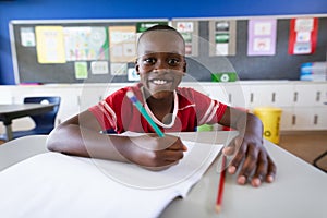 Portrait of african american boy smiling while sitting on his desk in the class at elementary school