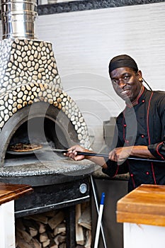 Portrait of african american chef man baking pizza in oven
