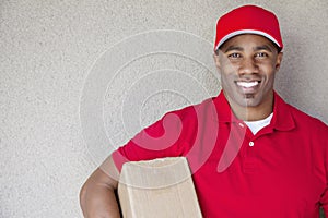 Portrait of a African American delivery man holding package against wall