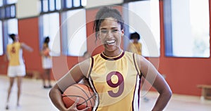 Portrait of african american female basketball player holding ball in indoor court, in slow motion