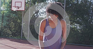 Portrait of african american female basketball player holding ball on sunny court, in slow motion