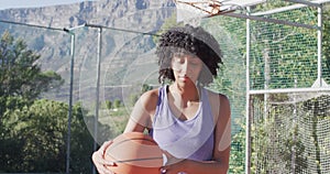 Portrait of african american female basketball player holding ball on sunny court, in slow motion