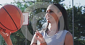 Portrait of african american female basketball player spinning ball on sunny court, in slow motion