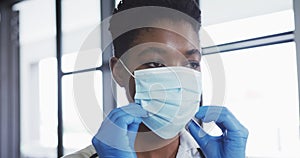 Portrait of african american female doctor wearing surgical gloves putting on face mask