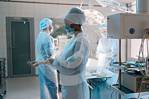 Portrait of African-American female nurse putting on disposable gloves as hygiene before surgery in hospital on