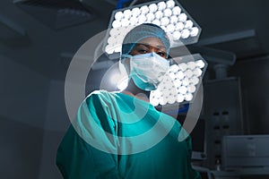 Portrait of african american female surgeon wearing surgical gown and face mask in operating theatre