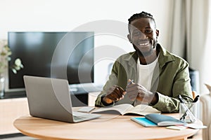 Portrait of african american freelancer guy sitting at desk at home office, looking at camera and smiling, free space