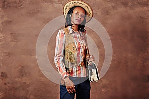 Portrait of an african american girl cowboy with hat and pistol in holster. photo in the studio. brown background
