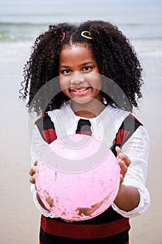 Portrait of African American girl smiling and holding a pink ball on the beach. Happy vacation holiday. Relaxation in vacation in