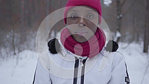 Portrait of african american girl standing in winter forest looking in camera close up. Beautiful girl in warm jacket