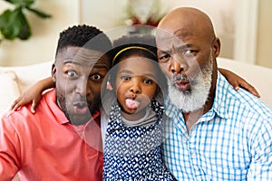 Portrait of african american grandfather, father and granddaughter making silly faces at home
