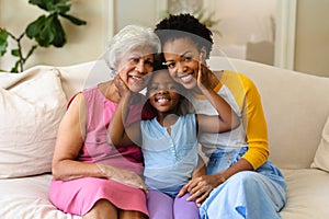Portrait of african american grandmother, mother and granddaughter smiling sitting on couch at home
