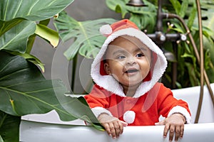 Portrait of African American little toddler baby girl in santa christmas dress smiling and playing inside the bathtub surrounding