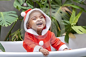 Portrait of African American little toddler baby girl in santa christmas dress smiling and playing inside the bathtub surrounding