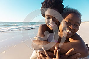 Portrait of african american loving young woman embracing senior mother at beach against sea and sky