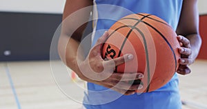 Portrait of african american male basketball player holding ball in indoor court, in slow motion