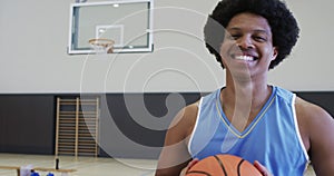 Portrait of african american male basketball player holding ball in indoor court, in slow motion