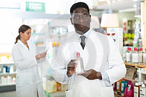 Portrait of african american male pharmacist in pharmacy demonstrating goods