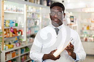 Portrait of african american male pharmacist in pharmacy demonstrating goods