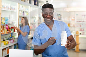 Portrait of african american male pharmacist in pharmacy demonstrating goods