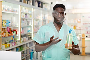 Portrait of african american male pharmacist in pharmacy demonstrating goods