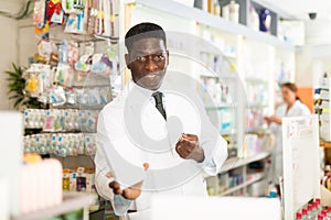 Portrait of african american male pharmacist in pharmacy demonstrating goods