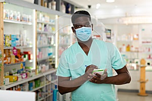 Portrait of an african american male pharmacist in a protective mask, makes important notes