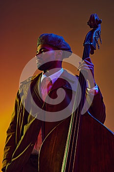 Portrait of African-American man, player with serene expression posing with string instrument in neon light against