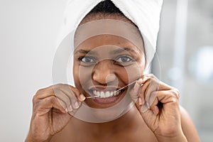 Portrait of african american mid adult woman using dental floss in bathroom