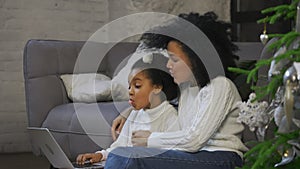 Portrait of African American mom and her little daughter communicate by video call using a laptop. Woman and girl